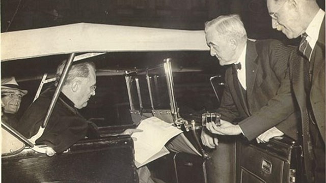 President sitting in car signing papers while three other men watch