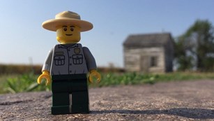 A lego ranger in front of the historic cabin at Homestead.