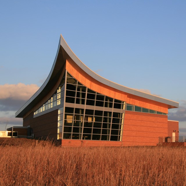 A plow-shaped building with lots of windows sits on the prairie.