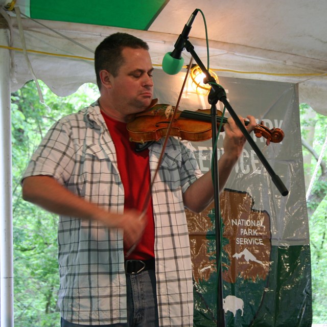 A man plays the fiddle while standing in front of a microphone.