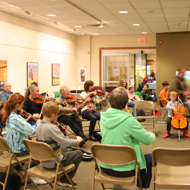 A group of people seated in a circle play the fiddle.
