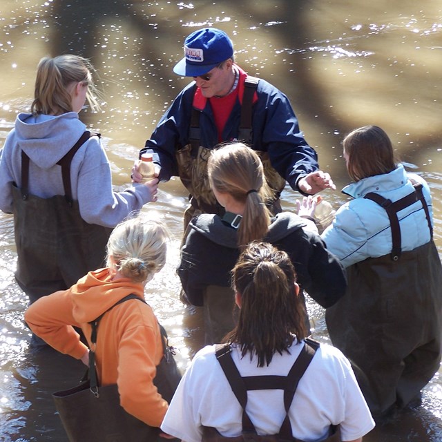 Volunteer helps students collect samples from Cub Creek