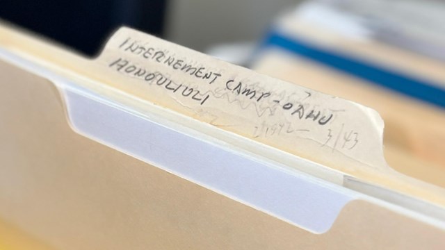 A hand taking a file named Internment Camp - Oahu Honouliuli out of a box