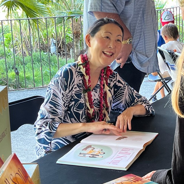 An Asian woman sitting at a table smiling at a visitor