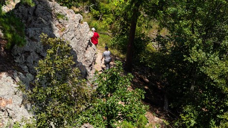 Two people hiking up a trail alongside textured geologic formations. 