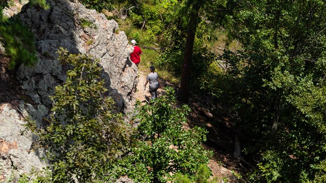 Two people hiking up a trail alongside textured geologic formations. 