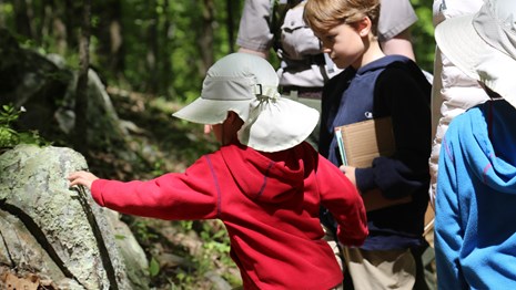 A young boy leans over and is touching a rock in the park.