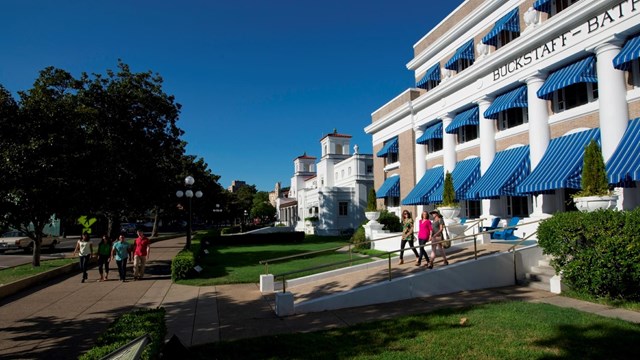 A couple walks out of a large building with blue awnings.