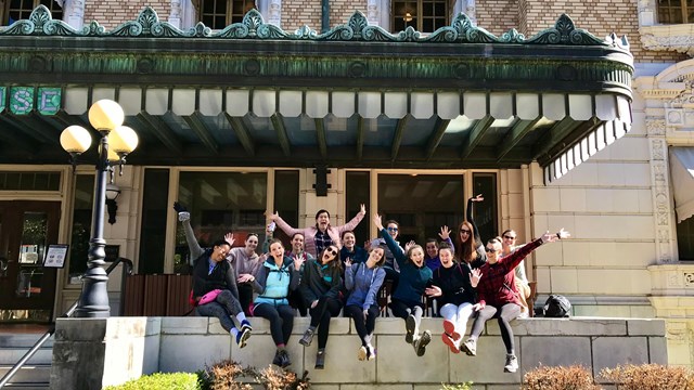 A group of people sit and pose ecstatically for a photo on a large porch.