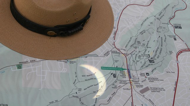 A partial eclipse shadow shines on a park map of Hot Springs next to a straw flat hat. 