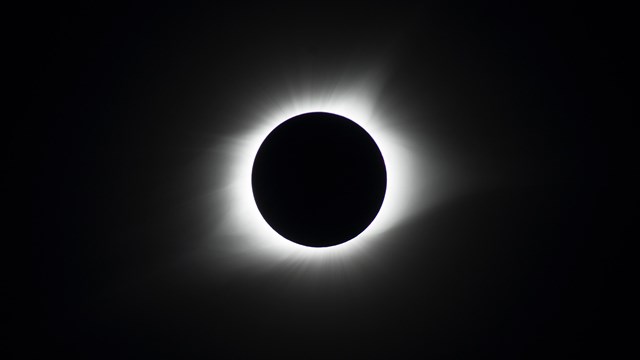 The sky and sun are pitch black; a ring of light radiates out from a dark circle in front of the sun