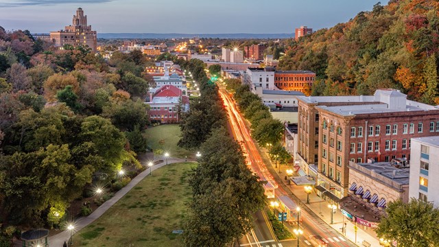 An aerial view looking down a light streaked highway between historic buildings in the evening.