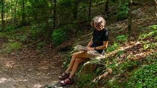 A woman sits on a rock and reading along Hot Springs Mountain