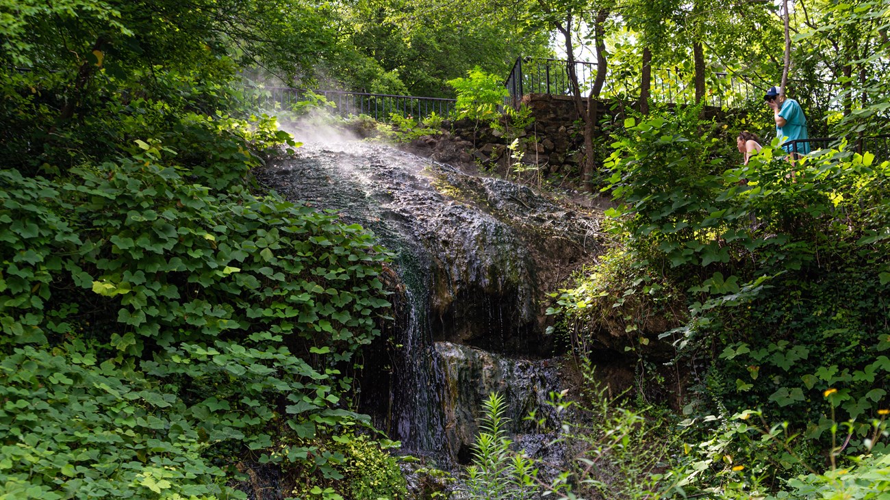 Thermal water cascades down a mossy hillside into two concrete collection pools.