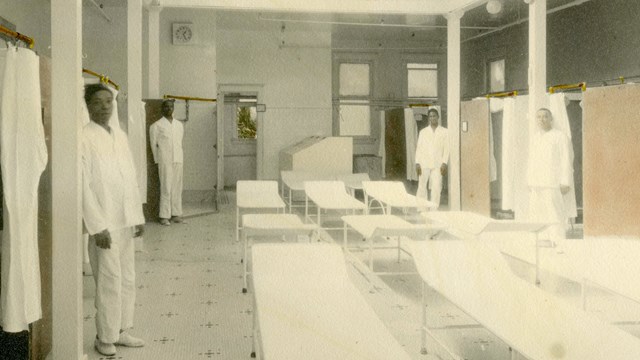 Four men stand in a bath hall surrounding benches