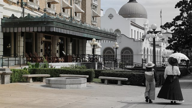 Two people in clothing from the late 1800s walk down Bathhouse Row.