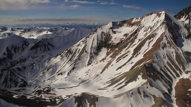 A ridge of jagged, snow capped mountains fills the sky line. 