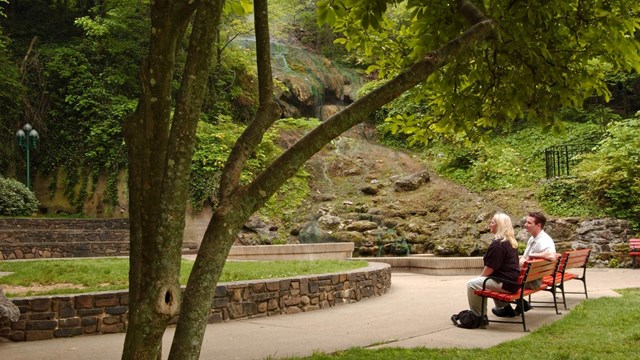 A couple sits on a park bench looking at the hot water cascade in the park.