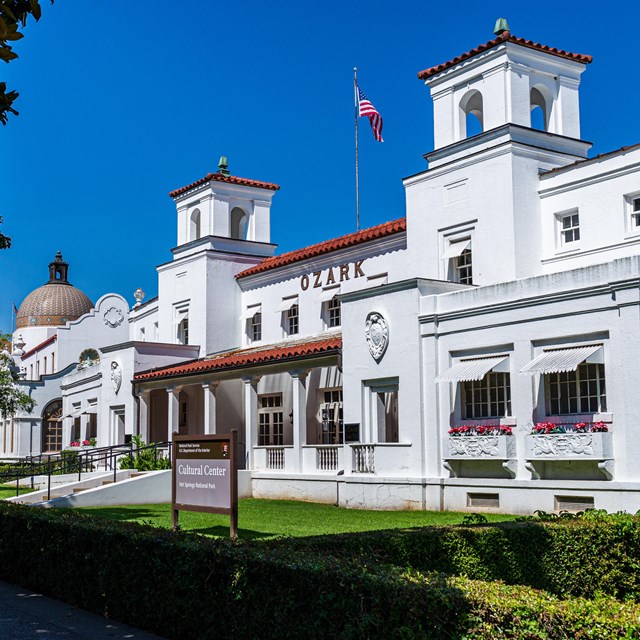 An active scene in front of the Fordyce Bathhouse; people sitting ,walking, and looking joyous.