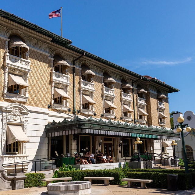 Front view of the Fordyce Bathhouse. Tan brick, a large green awning and porch adorn the buidling.