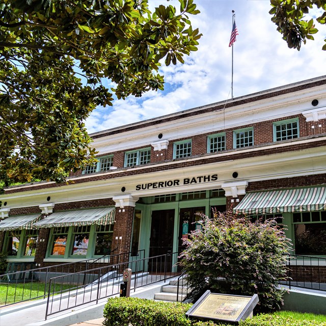 Front view of the red brick-laden Superior Bathhouse with green trim around the doors and windows.