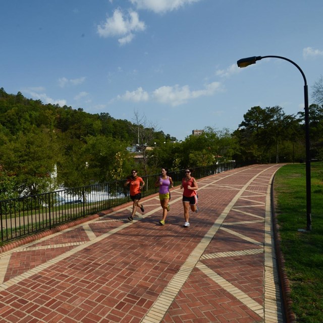 Three women running along a red brick path.