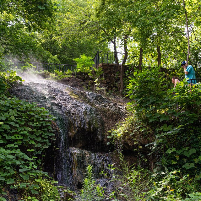 Thermal water cascades down a mossy hillside into two concrete collection pools.