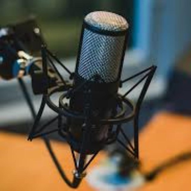 A microphone stand in the foreground with audio equipment in the background.