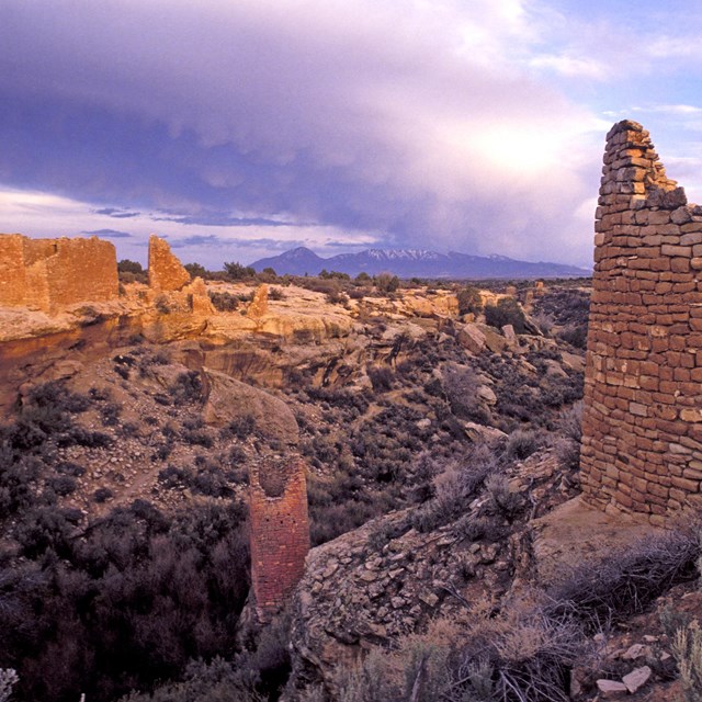 remains of stone structures around a canyon, purple sky behind