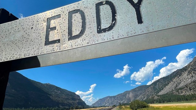 a sign with the word eddy has a green valley and railroad tracks heading into the distance