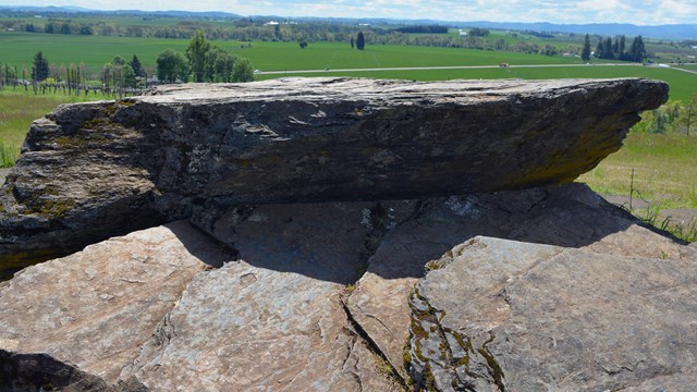 a flat boulder sits on a hill with a green valley in the background