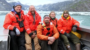 Photo of five members of an Alaska I&M network, seated on a boat in foul weather gear.