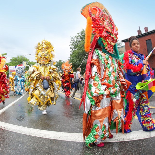In the street, costumed performers march in elaborate, colorful costumes 
