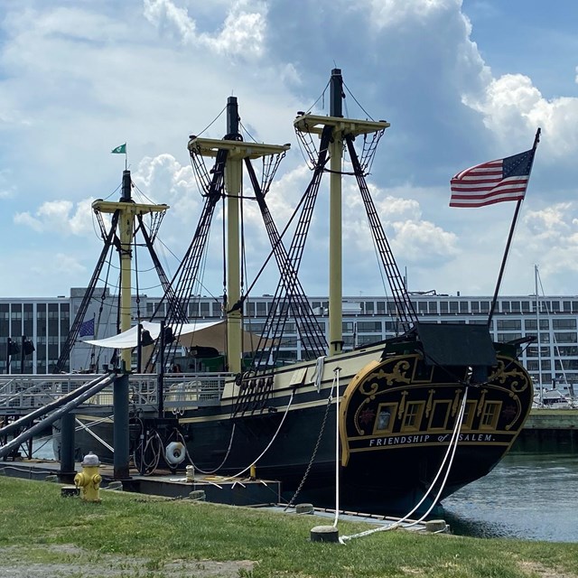 old wooden boat with american flag on the front and a modern building in the back