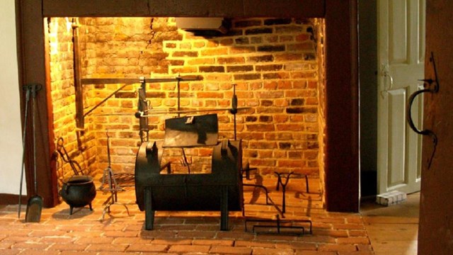 A brick fireplace in a room with a brick floor and an open door. 