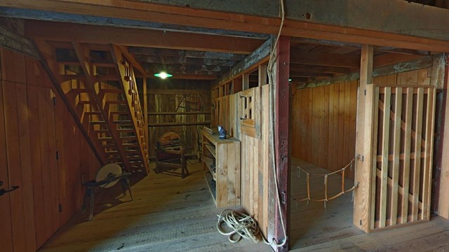 A dusty barn made of wood planks is mostly empty. A coil of rope sits on the floor next to a shelf.
