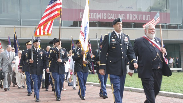 Color photo of men in military uniform marching near the National Constitution Center