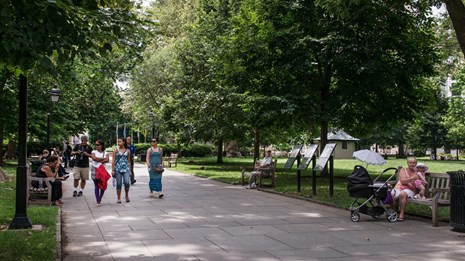 Color photo of people strolling along a tree-lined path in a park.