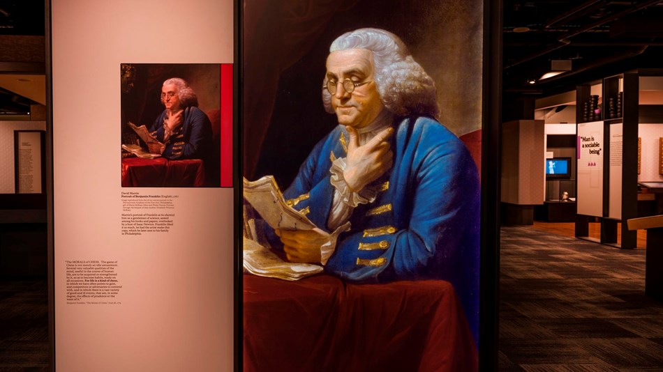 Color photo of an exhibit panel showing a portrait of Benjamin Franklin with museum exhibits behind.