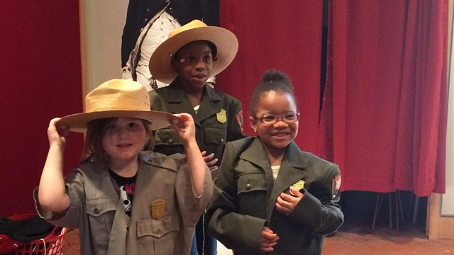 Color photo of three children trying on National Park Service uniforms.