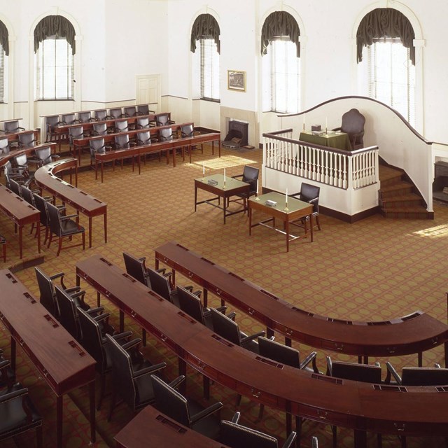 Color photo showing room with three rows of tiered seating facing a raised dias with a single chair.