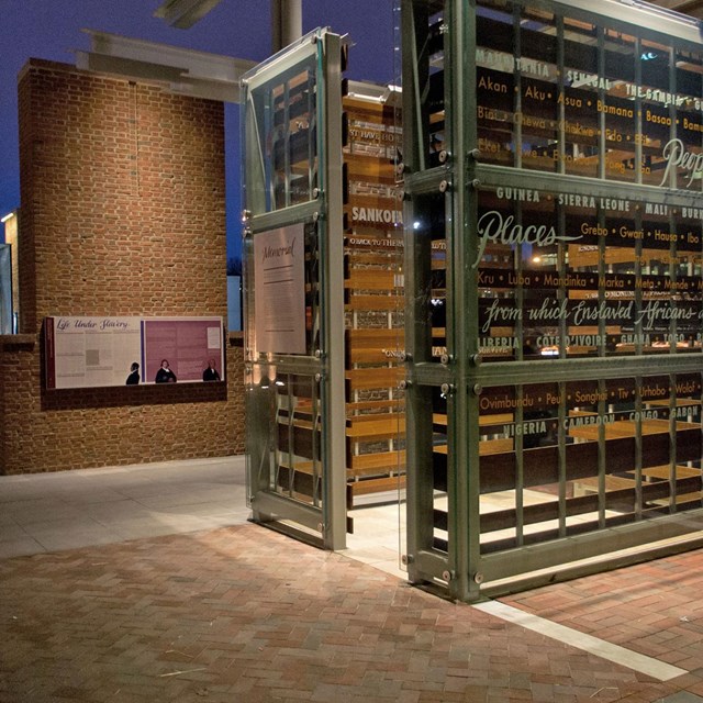 Color photo of outdoor exhibit showing glass enclosure and brick wall with exhibit panels.