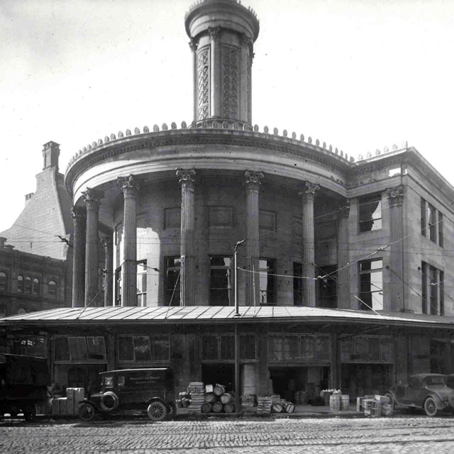 Black and white photo from the 1920's showing the large marble building with old vehicles near it.