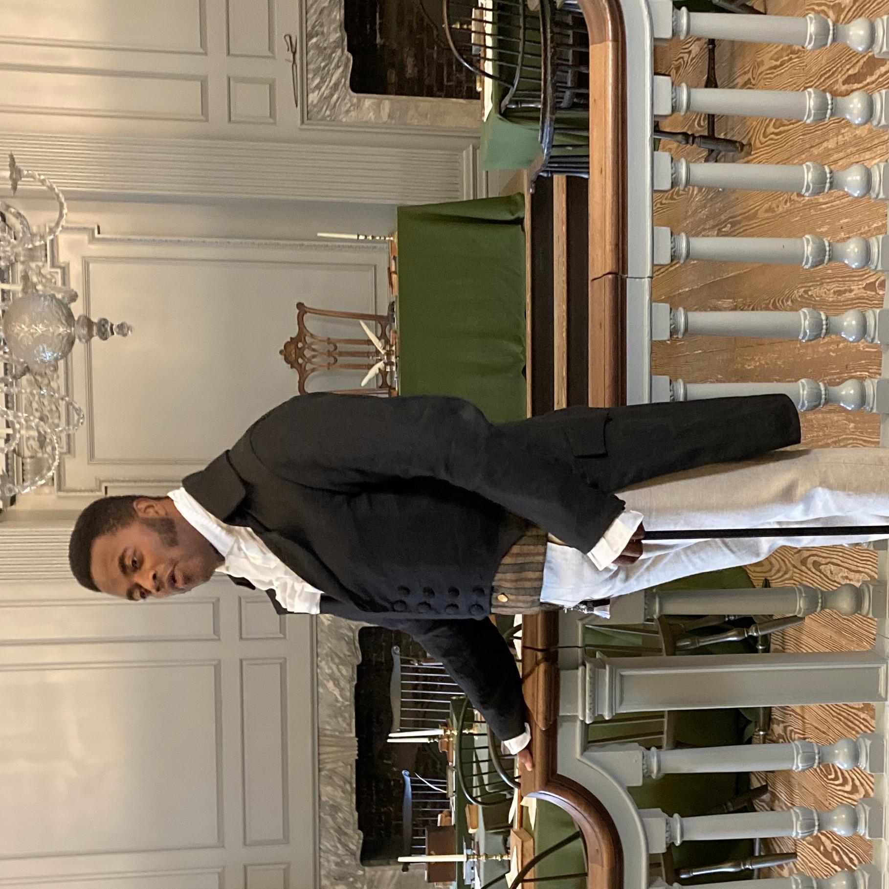 A man in clothing from the 1800s stands in the Assembly Room of Independence Hall.