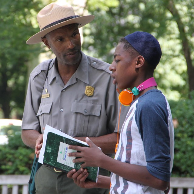 Color image showing a male park ranger and a teenage boy talking in an outdoor setting.