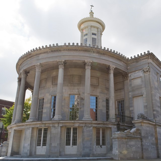 Color photo showing rounded facade of marble building with columns and a lantern tower.