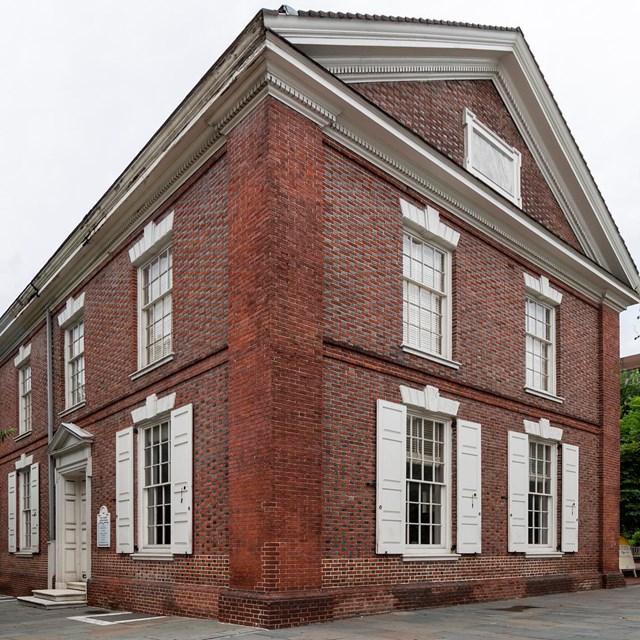 Color photo of two-story brick building on a street corner with windows framed by white shutters.