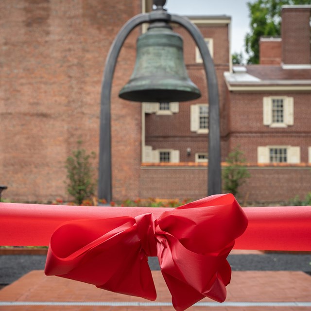 Red ribbon with bow with a large bell in the background