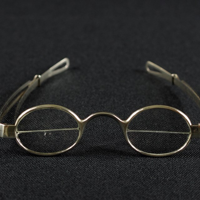 Color photo of 18th century bifocal eyeglasses against a black background.