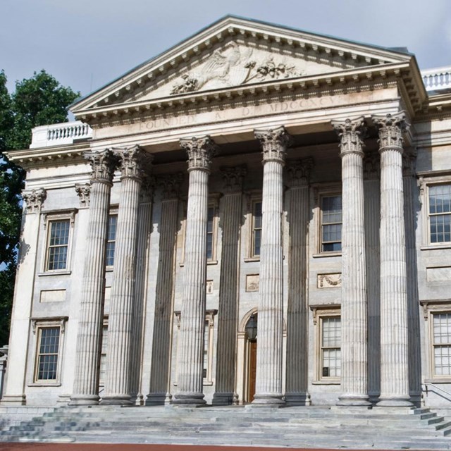 Color photo of a large two story building with triangular pediment supported by numerous columns.